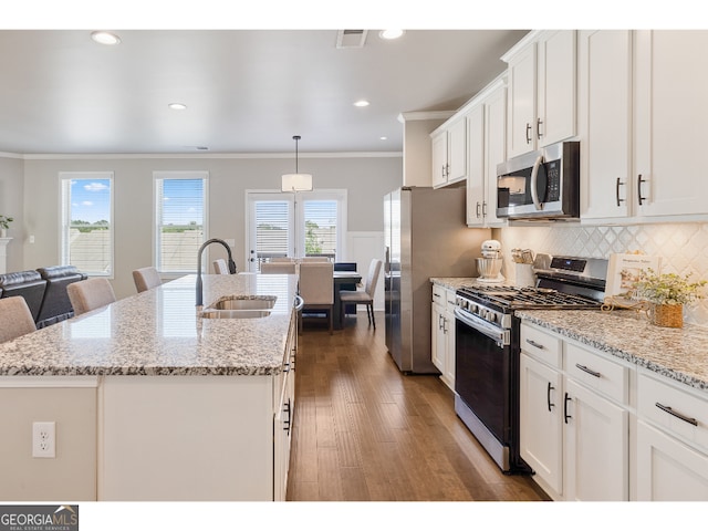 kitchen with light stone countertops, pendant lighting, appliances with stainless steel finishes, sink, and a center island with sink