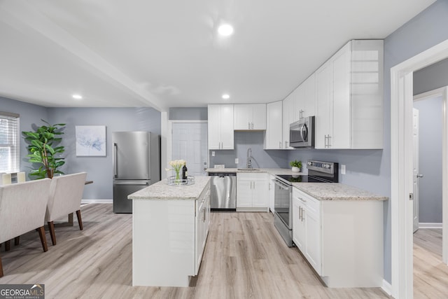 kitchen with sink, white cabinetry, light stone counters, a center island, and appliances with stainless steel finishes