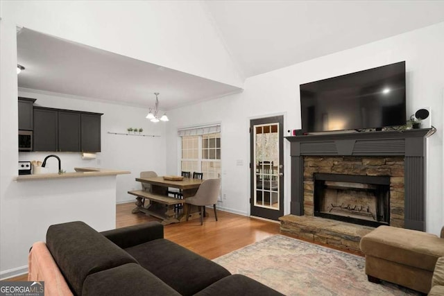 living room featuring a notable chandelier, a fireplace, light wood-type flooring, ornamental molding, and vaulted ceiling