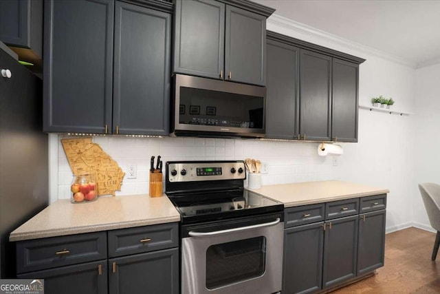 kitchen featuring hardwood / wood-style floors, gray cabinetry, decorative backsplash, ornamental molding, and stainless steel appliances