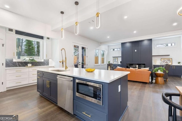 kitchen featuring pendant lighting, white cabinetry, stainless steel appliances, sink, and a center island with sink