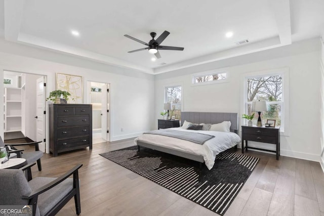 bedroom featuring ceiling fan, multiple windows, hardwood / wood-style flooring, and a raised ceiling