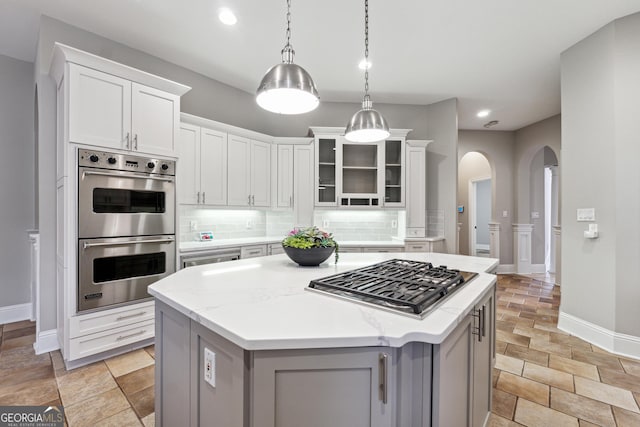 kitchen with white cabinetry, light stone counters, decorative light fixtures, a center island, and stainless steel appliances