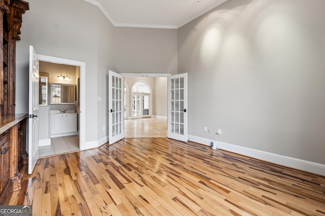 spare room featuring a high ceiling, ornamental molding, light hardwood / wood-style floors, and french doors