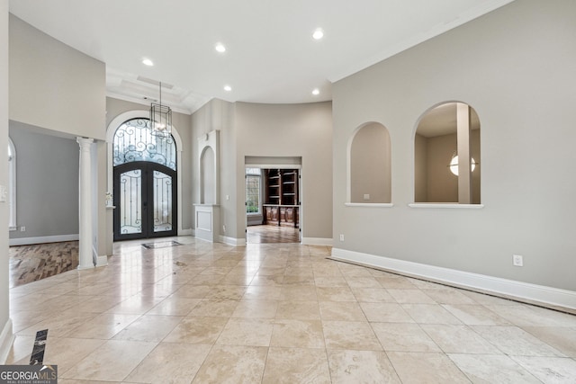 foyer with a towering ceiling, ornamental molding, french doors, and ornate columns