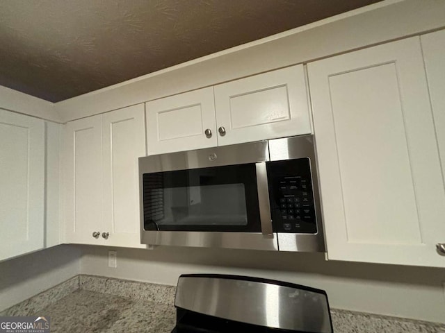 5449 Martins Crossing Rd, Stone Mountain, GA 30088 - kitchen view of stainless steel microwave, white cabinetry, light countertops, and a textured ceiling