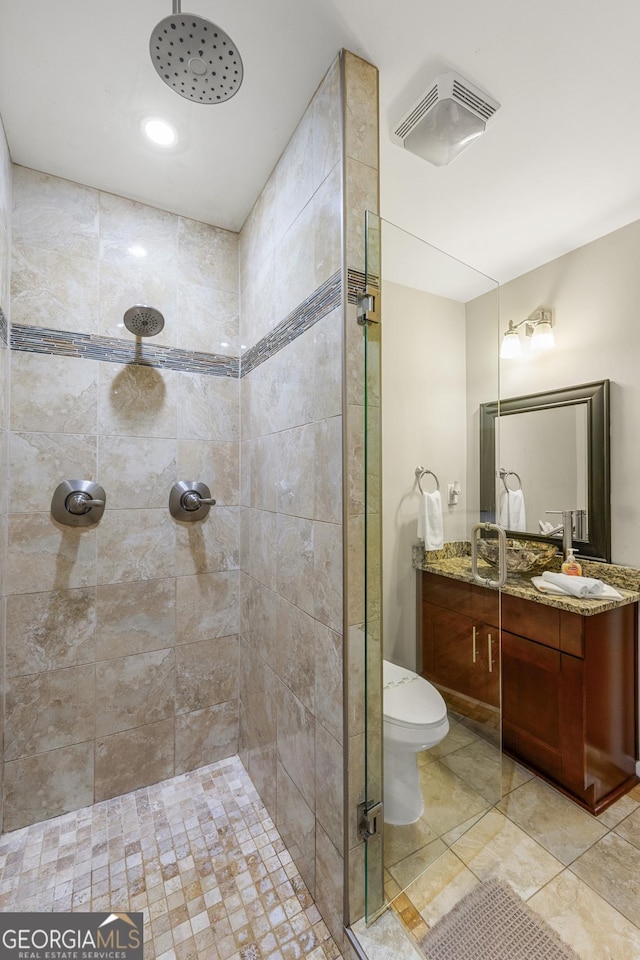 bathroom with a tile shower, toilet, and vanity