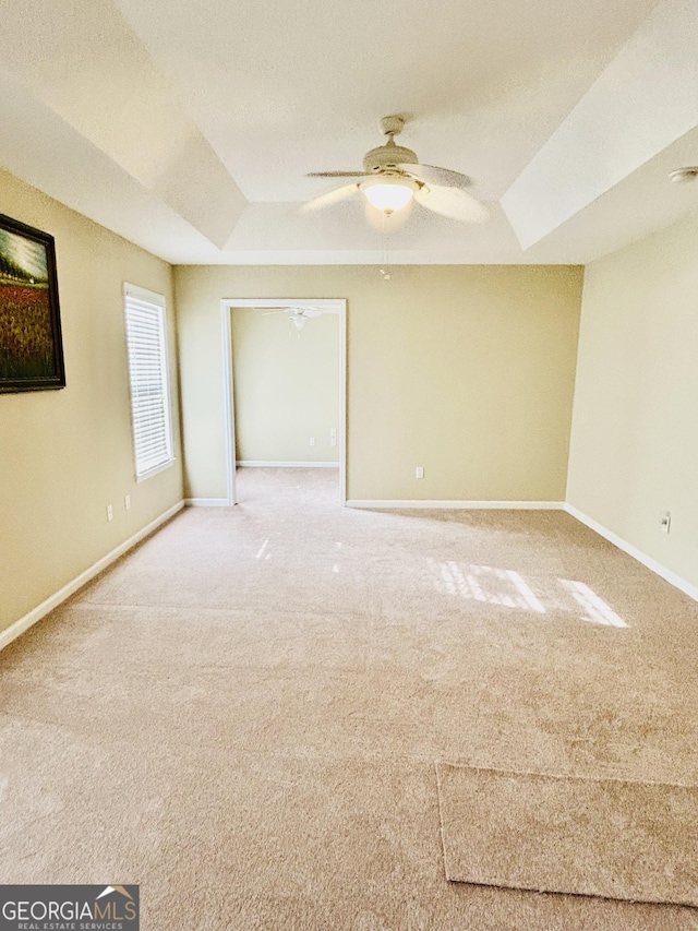 carpeted empty room with ceiling fan and a raised ceiling