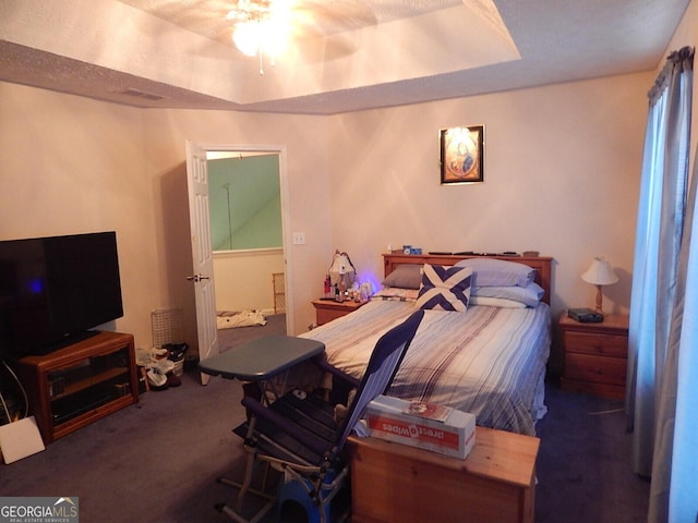 bedroom with ceiling fan, dark carpet, and a raised ceiling