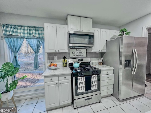 kitchen featuring white cabinets, tasteful backsplash, light tile patterned floors, light stone counters, and stainless steel appliances