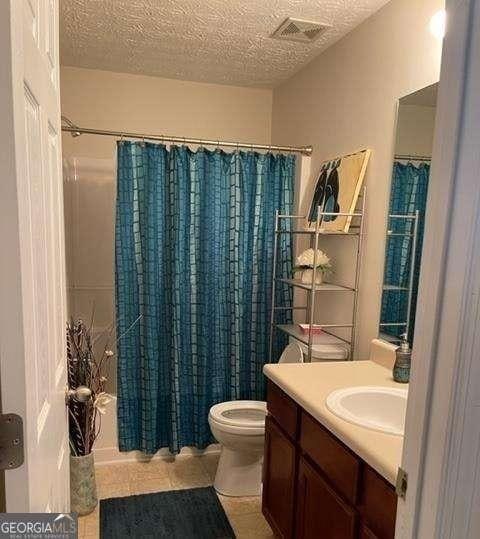 full bathroom with tile patterned floors, a textured ceiling, toilet, vanity, and shower / bath combo with shower curtain