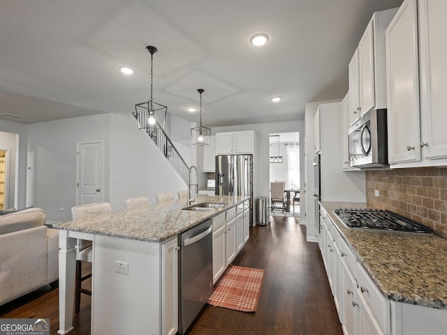 kitchen with pendant lighting, sink, white cabinetry, stainless steel appliances, and an island with sink