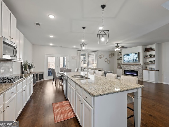 kitchen featuring pendant lighting, sink, white cabinets, stainless steel appliances, and a center island with sink