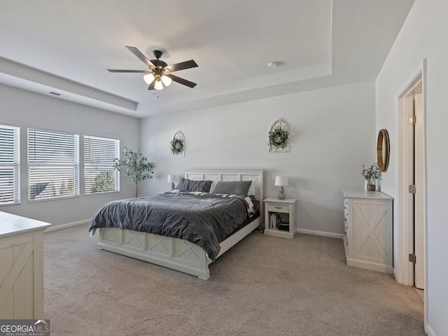 bedroom with light carpet, ceiling fan, and a tray ceiling