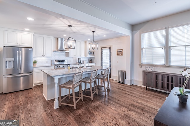 kitchen with white cabinets, a kitchen island with sink, stainless steel appliances, light stone countertops, and wall chimney exhaust hood