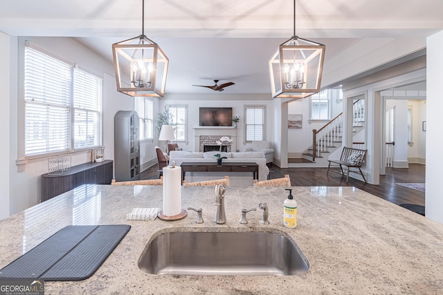 kitchen with pendant lighting, sink, a fireplace, and light stone countertops