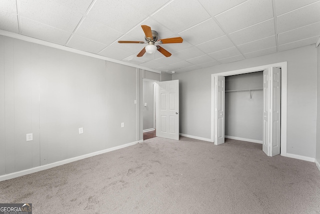 unfurnished bedroom featuring a closet, ceiling fan, carpet flooring, and a paneled ceiling