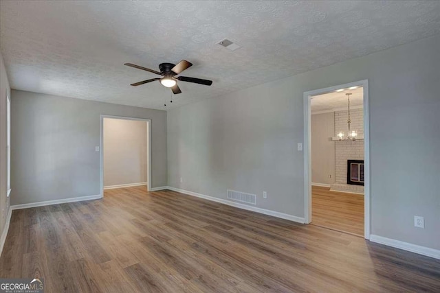 empty room featuring wood-type flooring, ceiling fan with notable chandelier, and a textured ceiling