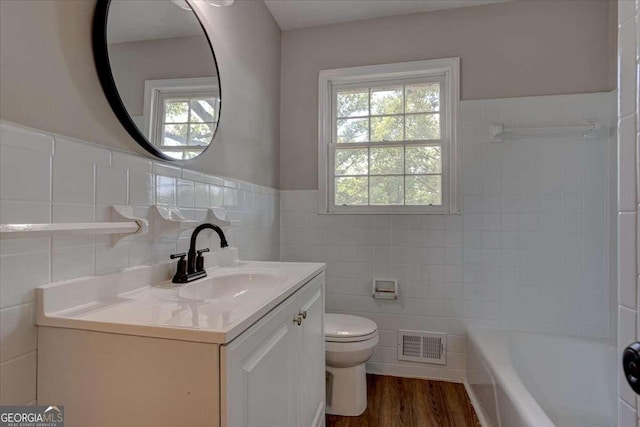 bathroom with a healthy amount of sunlight, hardwood / wood-style floors, tile walls, and vanity