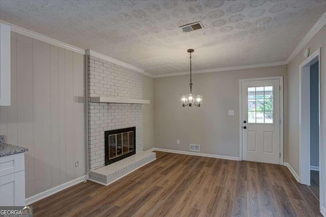 unfurnished living room with dark hardwood / wood-style floors, crown molding, a brick fireplace, a textured ceiling, and an inviting chandelier