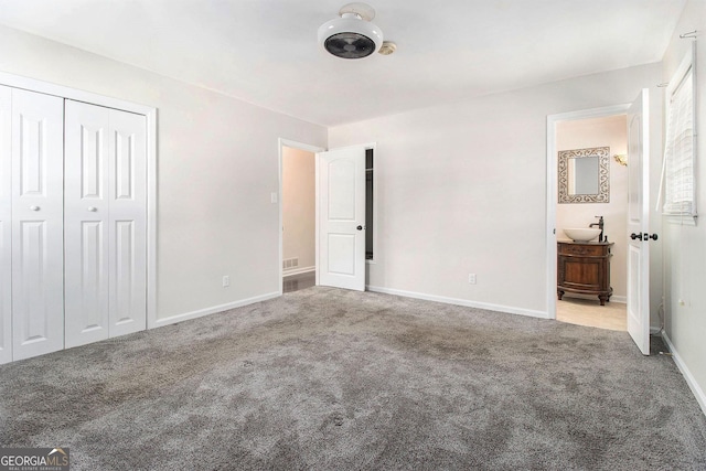 unfurnished bedroom featuring light colored carpet, ensuite bathroom, sink, and a closet