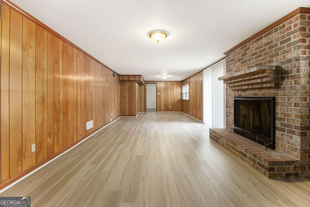 unfurnished living room with ornamental molding, a fireplace, light hardwood / wood-style floors, and wood walls