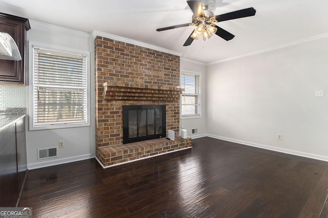 unfurnished living room featuring a brick fireplace, ornamental molding, dark hardwood / wood-style floors, and ceiling fan