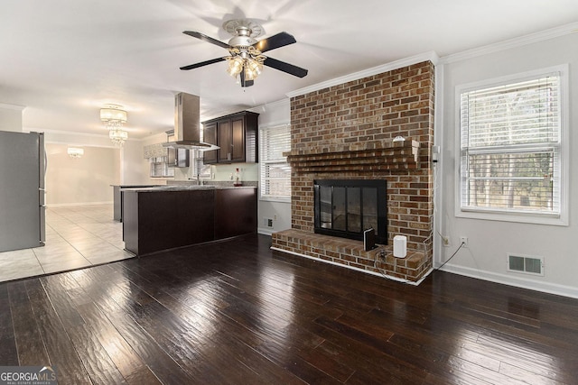 unfurnished living room with crown molding, ceiling fan, hardwood / wood-style floors, and a brick fireplace