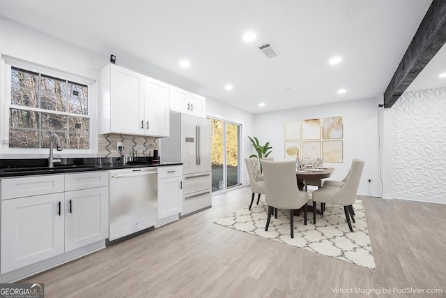 kitchen with sink, dishwashing machine, white cabinets, light hardwood / wood-style floors, and backsplash