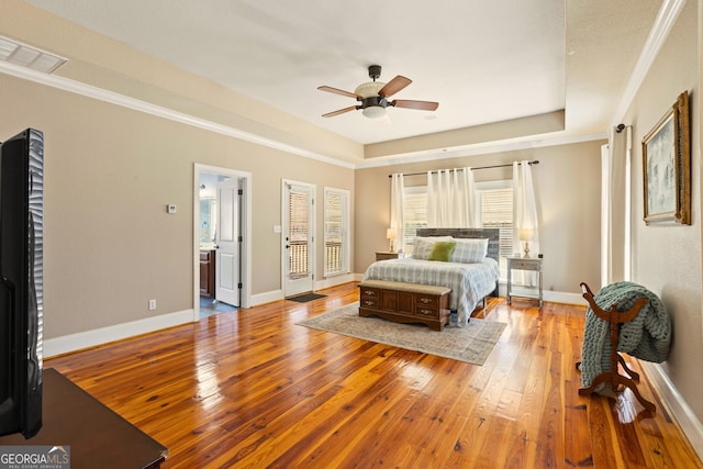 bedroom featuring connected bathroom, ornamental molding, ceiling fan, a tray ceiling, and light hardwood / wood-style flooring