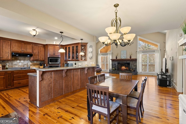 kitchen featuring stainless steel microwave, a fireplace, light wood-type flooring, backsplash, and a breakfast bar area