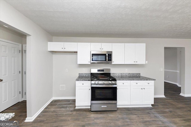 kitchen featuring stainless steel appliances, white cabinetry, dark stone counters, and a textured ceiling