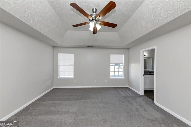 carpeted empty room featuring ceiling fan, a raised ceiling, and a textured ceiling