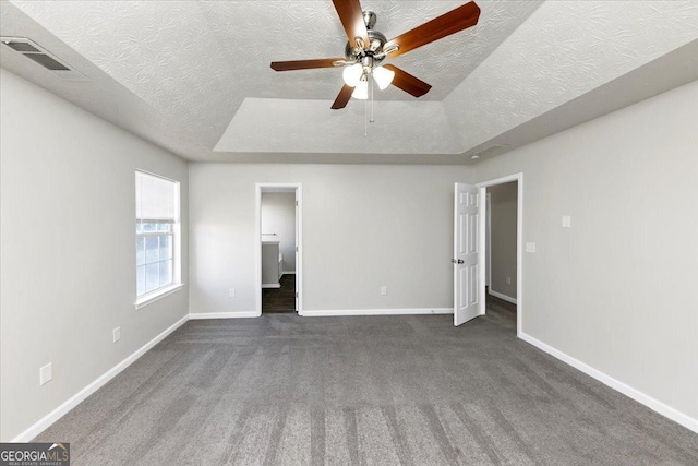 unfurnished bedroom with dark carpet, a textured ceiling, a tray ceiling, and ceiling fan