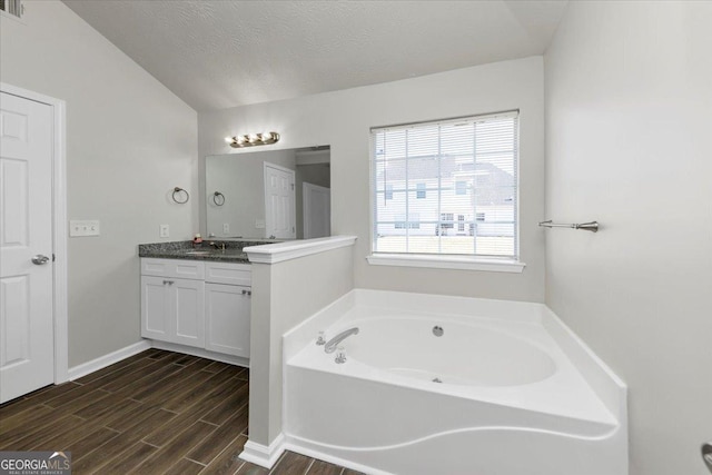 bathroom with vanity, a bath, a textured ceiling, and lofted ceiling