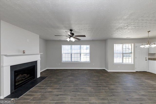 unfurnished living room featuring ceiling fan with notable chandelier, plenty of natural light, a textured ceiling, and dark hardwood / wood-style flooring