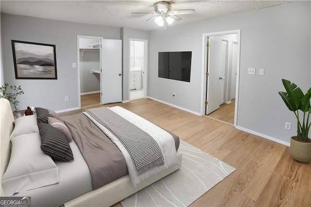 bedroom with a textured ceiling, a walk in closet, light wood-type flooring, ceiling fan, and connected bathroom