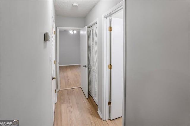 hallway with light wood-type flooring and a textured ceiling