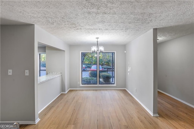 unfurnished dining area with a textured ceiling, a chandelier, and light hardwood / wood-style flooring