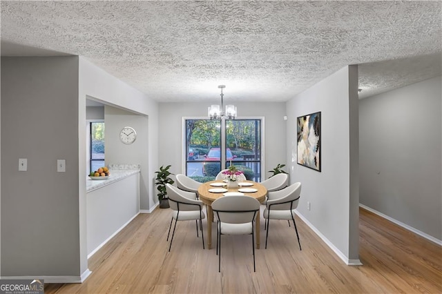 dining area featuring a textured ceiling, light wood-type flooring, a chandelier, and a healthy amount of sunlight