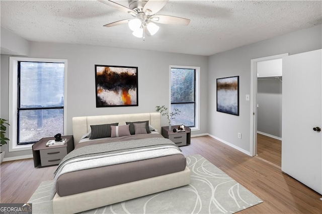 bedroom featuring light hardwood / wood-style flooring, ceiling fan, a textured ceiling, a spacious closet, and a closet