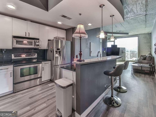 kitchen featuring a center island, appliances with stainless steel finishes, white cabinets, light wood-type flooring, and pendant lighting