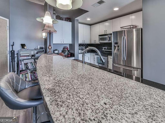 kitchen featuring pendant lighting, white cabinets, stainless steel appliances, dark stone counters, and a kitchen breakfast bar