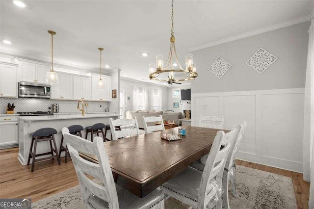 dining room with light hardwood / wood-style floors, ornamental molding, and a notable chandelier