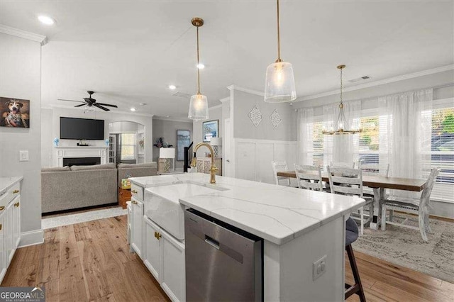 kitchen with dishwasher, white cabinets, sink, decorative light fixtures, and a center island with sink