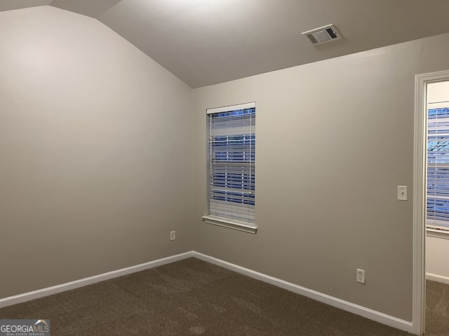 spare room featuring dark colored carpet and vaulted ceiling