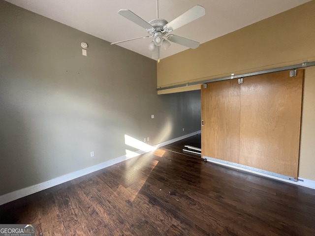 empty room with dark wood-type flooring, ceiling fan, a barn door, and vaulted ceiling