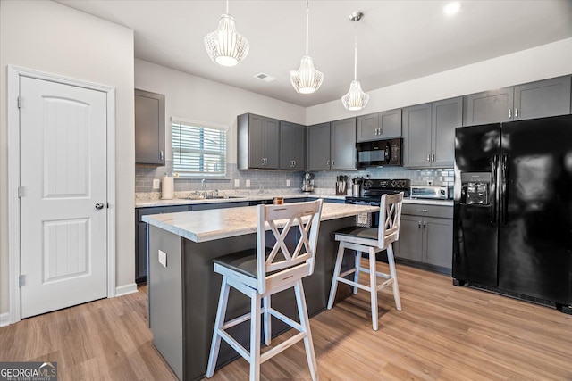 kitchen with a breakfast bar area, decorative light fixtures, a kitchen island, light hardwood / wood-style floors, and black appliances