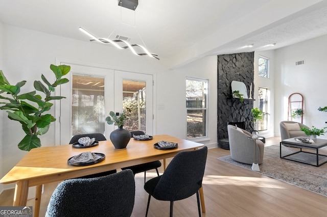 dining space with french doors, a textured ceiling, a stone fireplace, and light wood-type flooring