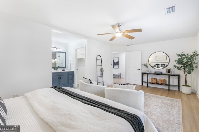 bedroom featuring light hardwood / wood-style floors, a spacious closet, ensuite bath, and ceiling fan